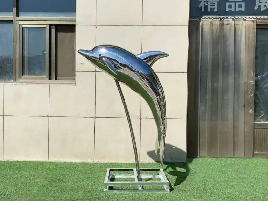 A mirror-finished forged stainless steel sculpture of a diving dolphin on a curved stand, emphasizing graceful anatomical curves and aquatic aesthetics.