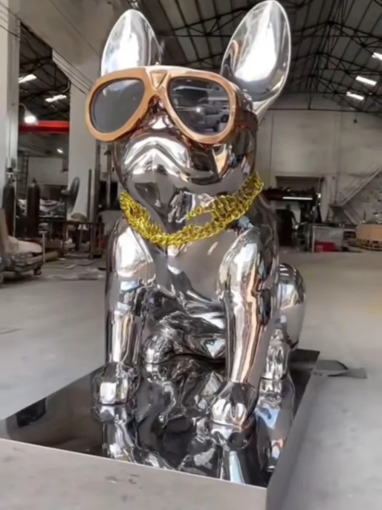 Finished mirror-polished stainless steel French Bulldog statue featuring fashion sunglasses and a gold chain, displayed in the factory.