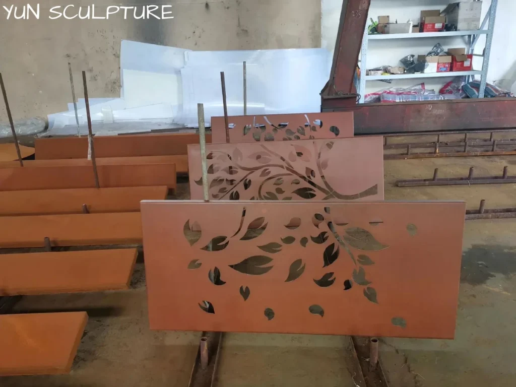 A modern mild steel wall panel standing in a workshop, showcasing a complex laser-cut botanical leaf pattern with sharp, accurate edges.