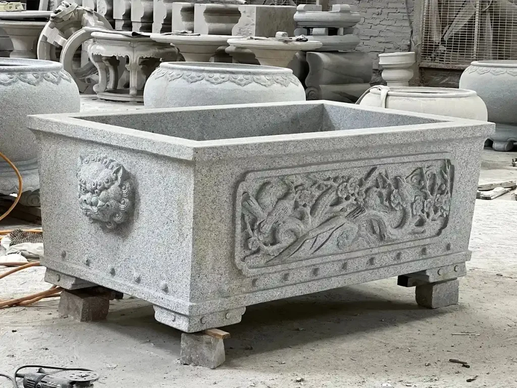 A large rectangular granite stone planter featuring detailed hand-carved lion head and cloud motifs, ready for installation in a modern architectural landscape.