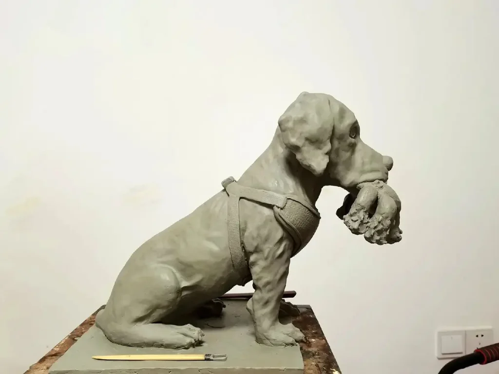 Side view of a Labrador clay model being refined, showing the hunting vest harness and bird details.