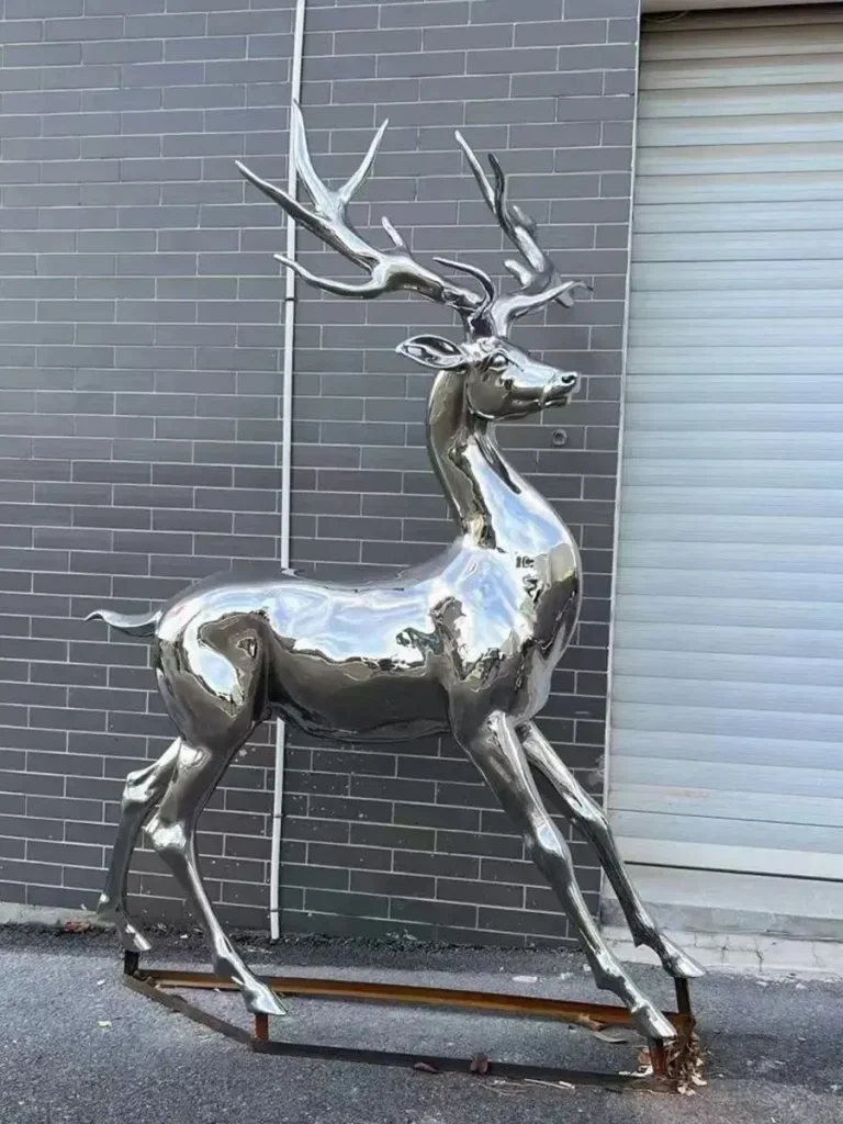Side view of a smooth mirror stainless steel deer sculpture. Its reflective surface and clean lines create a striking visual contrast in a modern garden.