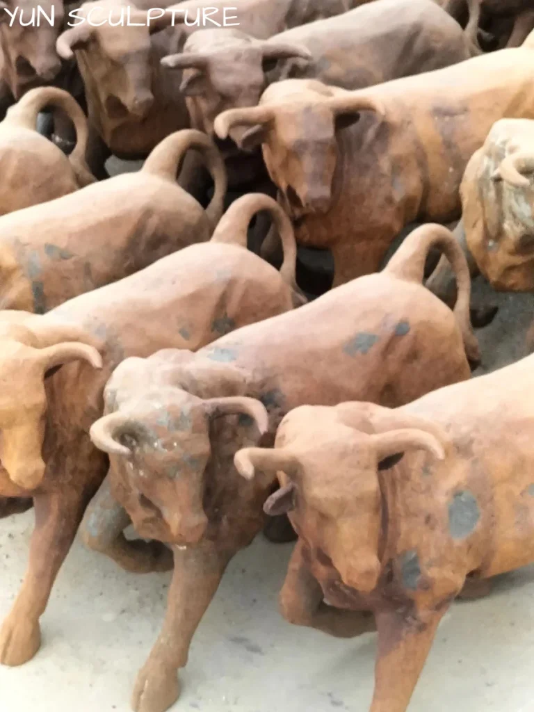 A group of cast iron bull statues with a rusted finish in a workshop yard, illustrating the type of outdoor garden art that requires annual inspection and rust converters to maintain its condition.