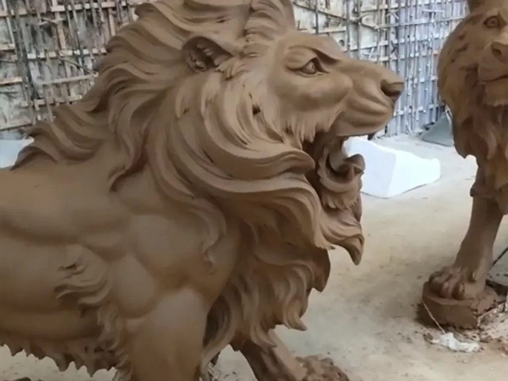 Close-up of a clay lion maquette showing the intricate undulating shoulder muscles and thick, layered mane. This detailed prototyping phase is essential before casting molten metal to ensure the highest level of anatomical accuracy in the final bronze piece.