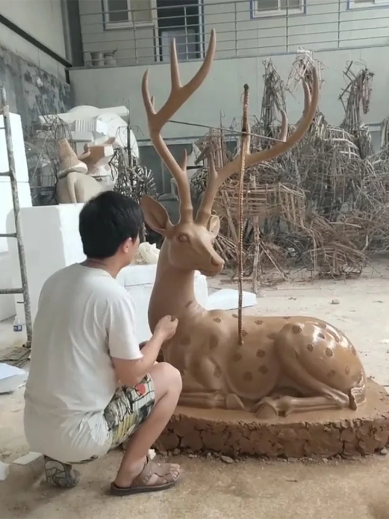 A sculptor meticulously refining the clay model of a majestic stag in a workshop. This essential first step in the ancient lost-wax casting method allows the artist to capture delicate anatomical details, such as muscle tension and graceful branching antlers, before the bronze is poured.