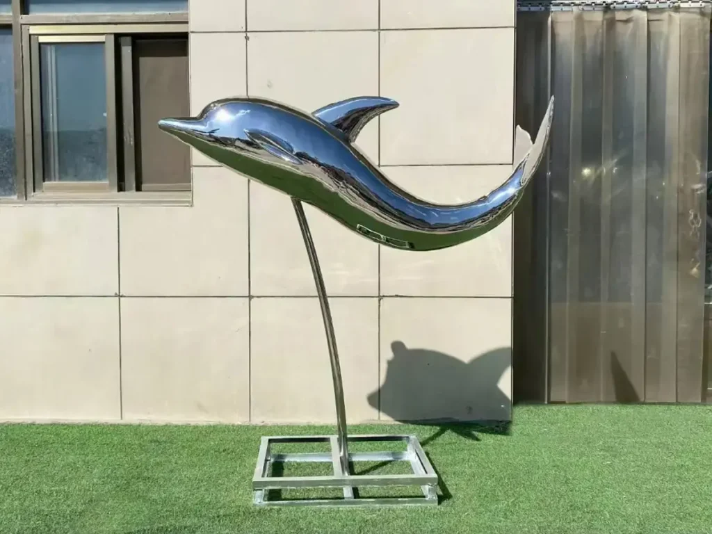 A smooth, highly polished forged stainless steel sculpture of a dolphin leaping upward, showcasing seamless welding and a flawless mirror finish.