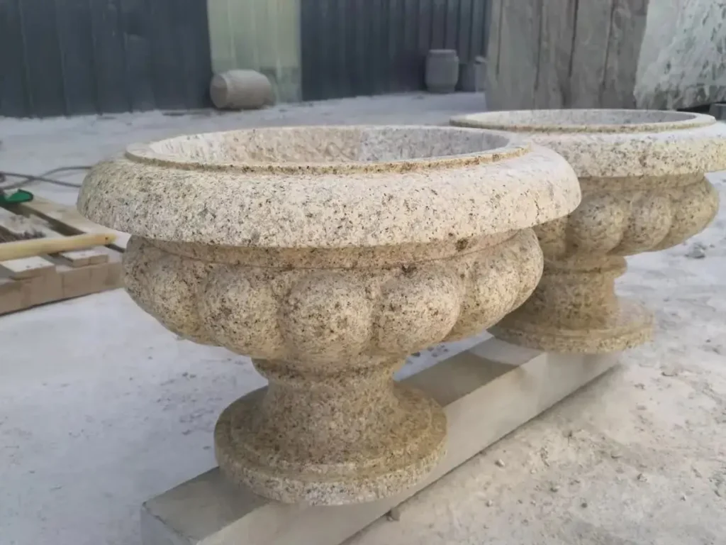 Two circular solid rock planters carved from natural granite, showing the low-porosity texture that makes them ideal for all-weather outdoor use.