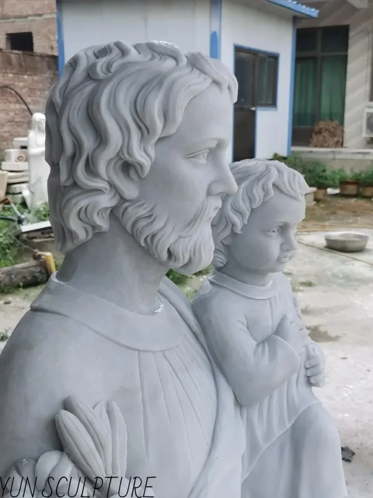 An angled side profile of a beautifully carved white marble St. Joseph and Child Jesus statue, highlighting the flowing drapery and the protective embrace. This classic representation serves as a powerful visual contrast to the sleeping st joseph statue, emphasizing the traditional gestures of fatherly guardianship that are intentionally absent in the resting figure.