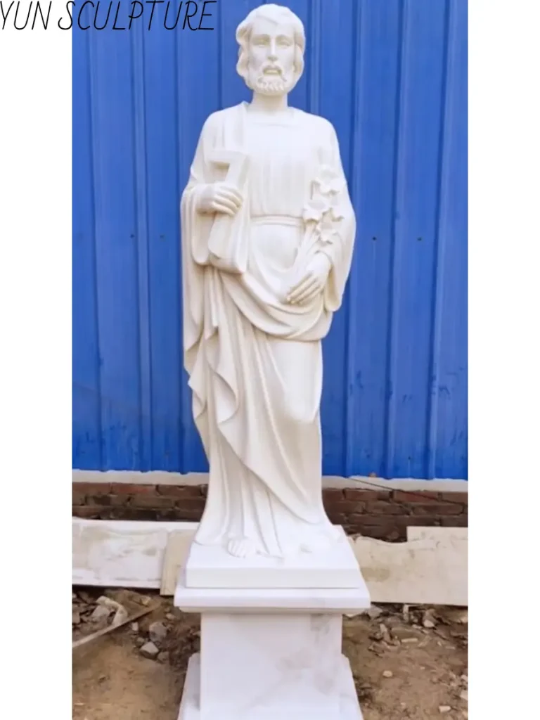 A standing white marble statue of Saint Joseph holding a lily, representing his structural and protective role in the Holy Family.