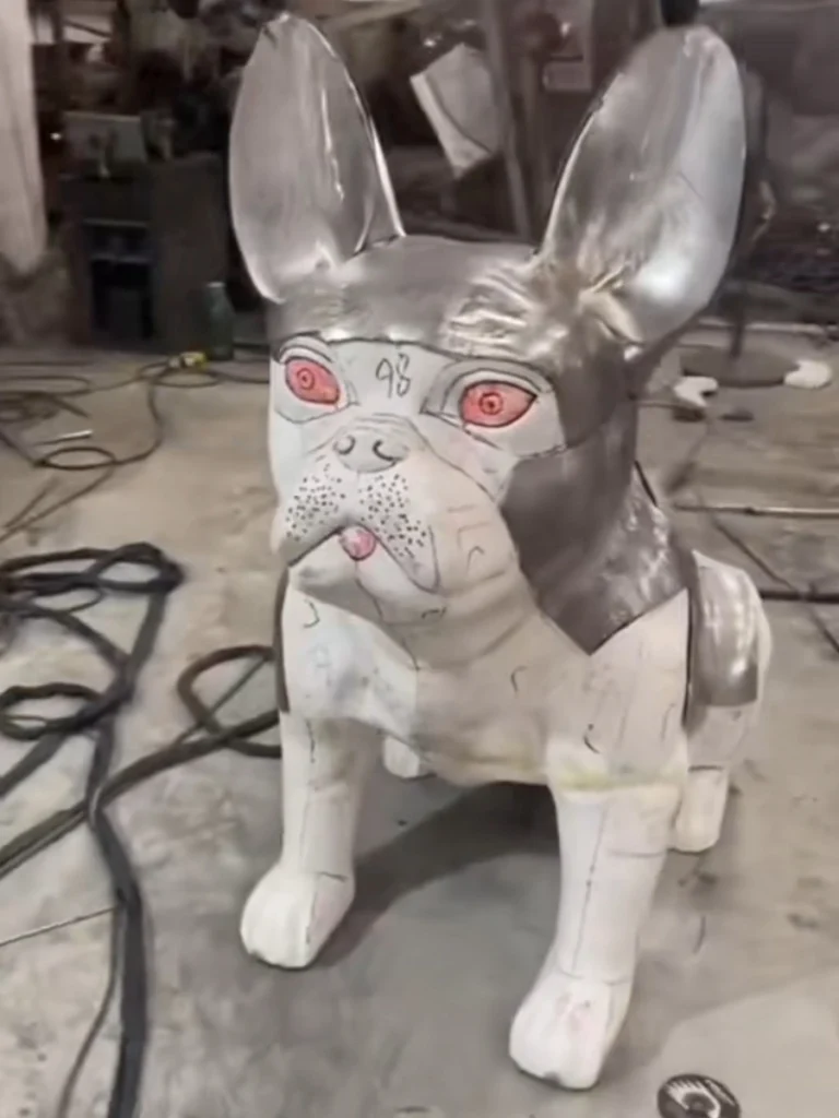 Fabrication process of a metal dog statue showing raw stainless steel plates welded together before grinding and polishing.