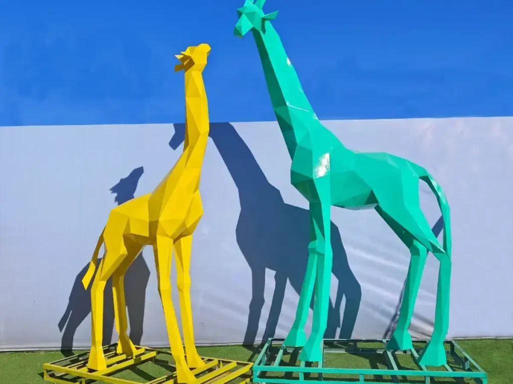 Two towering geometric giraffe statues made of painted stainless steel in bright yellow and green. Their sleek, faceted design and extreme height perfectly illustrate how vertical sculptures extend the visual height of a landscape and create an elegant vertical rhythm.