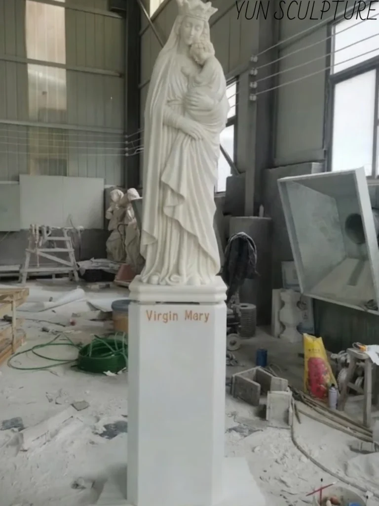 Side profile of a Virgin Mary statue holding baby Jesus, mounted on a custom-inscribed pedestal, highlighting the flowing drapery and structural balance.