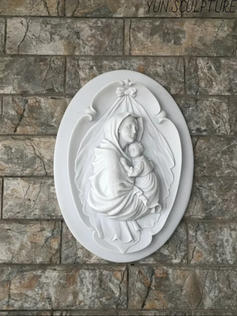 An elegant white marble Madonna and Child relief sculpture beautifully mounted on a textured exterior stone wall.