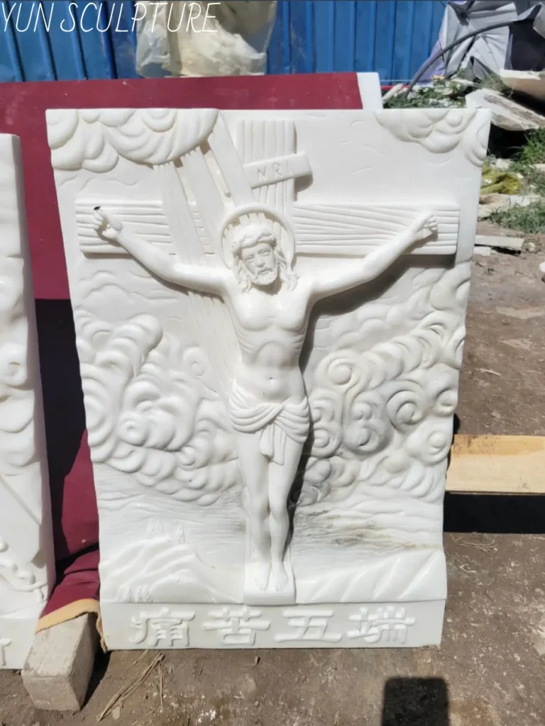 A magnificent white marble jesus on cross statue relief, masterfully hand-carved in a sculptor's workshop. Often commissioned as the devotional heart of the entire narrative—such as the poignant eleventh station—this deep stone relief features intricate swirling clouds behind the crucified figure, demonstrating the exquisite craftsmanship required to capture the intense theology of suffering and sacrifice.