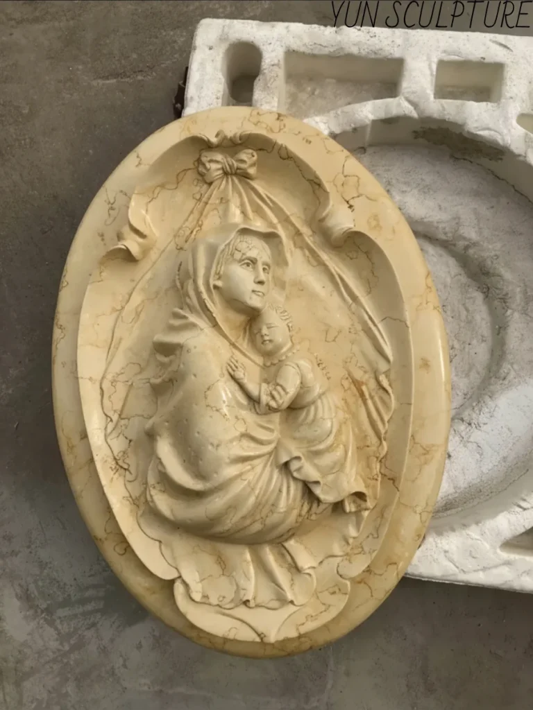 A commissioned yellow marble bas-relief of the Madonna and Child, shown in the sculpture studio alongside its protective casting mold.