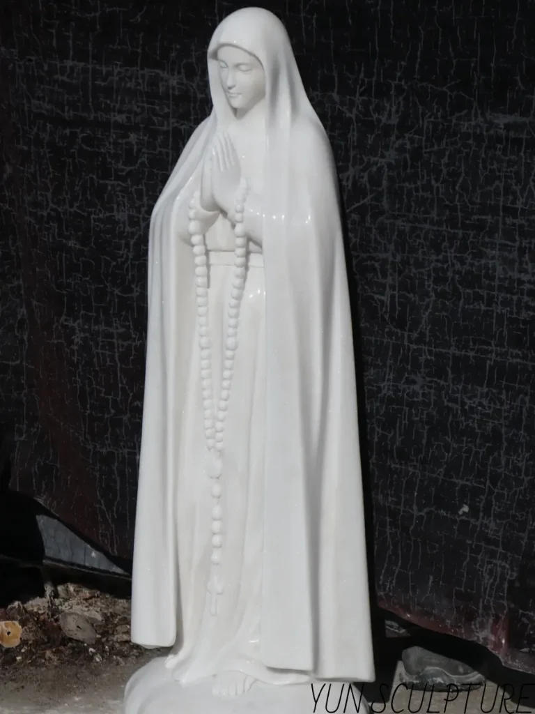 An angled, full-length shot of a heavy, 5-foot tall white marble religious monument in a sculptor's studio. Because wind resistance increases dramatically at this nearly life-size scale, expert engineering calculations, internal reinforcement, and proper base design are absolutely essential to guarantee foundation stability and long-term safety for the heart of a parish courtyard.
