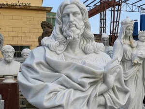 A prominent large white marble Jesus bust statue with intricate details is displayed in a busy sculpture workshop, with a smaller crowned statue and an Aristotle bust in the background.