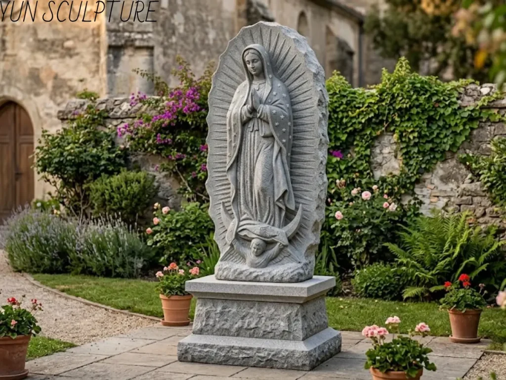 A monumental, hand-carved natural stone Custom Our Lady of Guadalupe statue standing majestically on a heavy pedestal in a blooming, historic church courtyard. Showcasing the successful final stage of our DDP global shipping and expert installation guidance, this breathtaking monument demonstrates the seamless transition from our factory to your sacred ground, perfectly ensuring the artwork stands with enduring faith, dignity, and structural stability for generations.