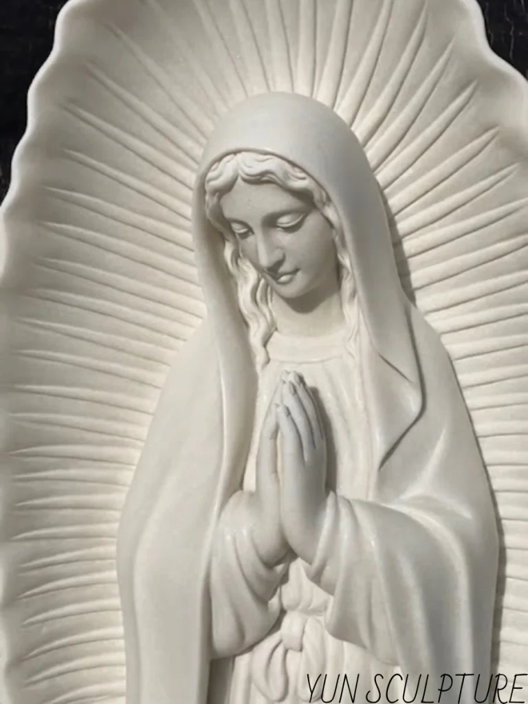 An extreme close-up of a hand-carved white marble Virgin of Guadalupe statue, highlighting her serene face and hands joined in prayer. The exceptionally detailed, sunburst-like luminous mandorla aura radiating behind her is shaped manually with artistic precision, demonstrating how expert stone carving deeply respects both the fragile marble material and the profound sacred symbolism.