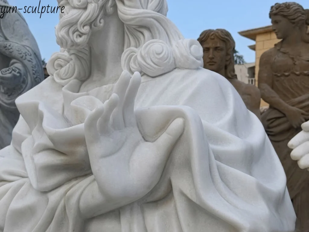 A masterful close-up of a white marble Jesus statue, focusing on His gently raised hand and the deeply carved, fluid drapery of His robes. This exquisite detailing perfectly illustrates the Renaissance Tradition's return to naturalism and human beauty, capturing Christ's approachable humanity made manifest in solid stone.