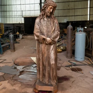 A life-size bronze Jesus statue with a crown of thorns and intricate floral patterns on his robe, standing in our foundry. This contemplative and solemn statue possesses a quiet spatial personality, ideal for reflective church gardens or private prayer spaces.