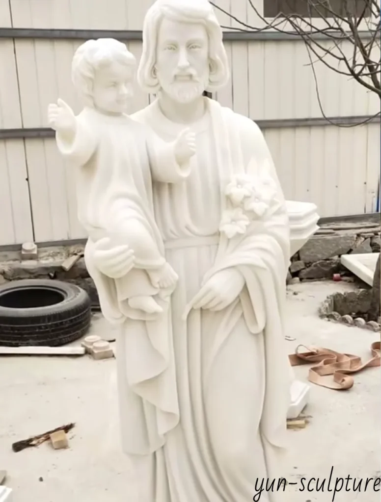 A hand-carved white marble statue of Saint Joseph holding the Child Jesus, representing the profound relationship of fatherhood and mentorship described in the Gospel of Luke.