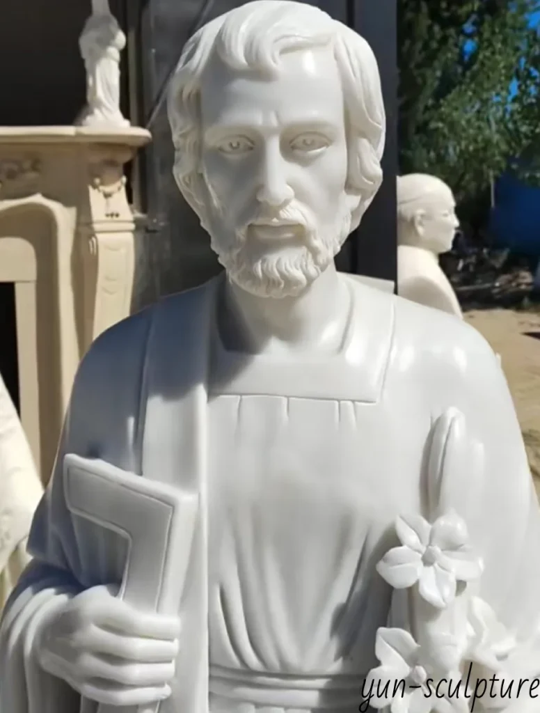 A close-up of a white marble St. Joseph the Worker statue, showing his calm, focused facial expression and hand holding a carpenter's square, illustrating high-precision carving of professional tools.