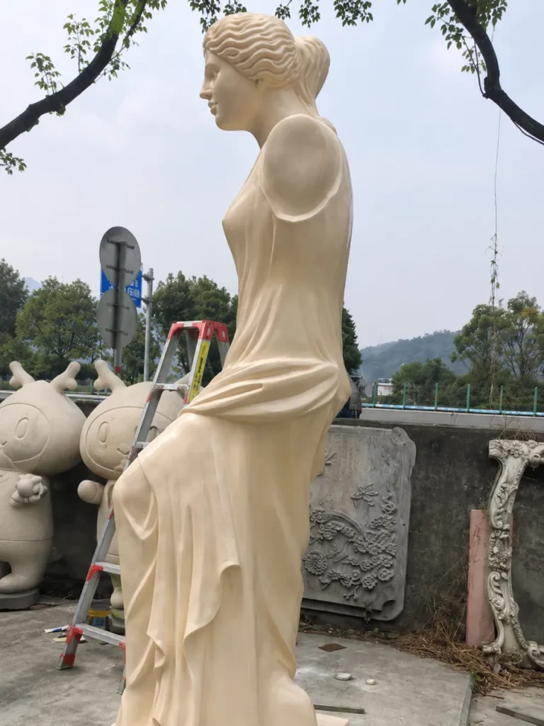 Side profile of a hand-carved cream marble Venus de Milo, showcasing the elegant spiral composition that requires an appropriate viewing distance to be fully appreciated in a garden setting.