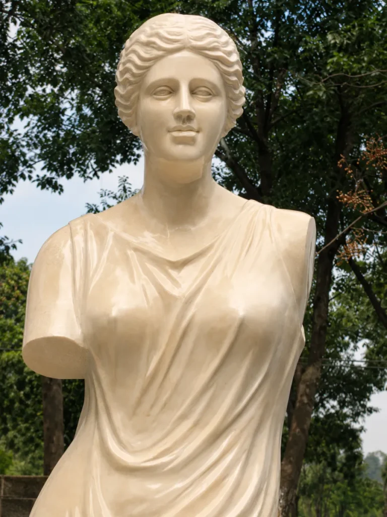 Close-up of the torso and drapery of an Egyptian Beige marble sculpture. The hand-carved stone planes reflect light beautifully, making it an ideal durable choice for gardens in the American South or Mediterranean climates.