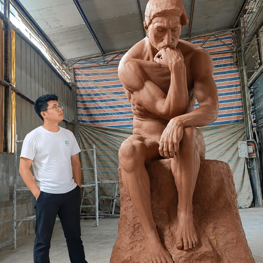 Master sculptor Donghui Zhang examining a 1:1 scale clay model of Rodin's The Thinker. The model accurately captures the complex torsion of the torso caused by the right elbow resting on the left thigh, ensuring the muscular tension and psychological depth of the original masterpiece are preserved before casting.