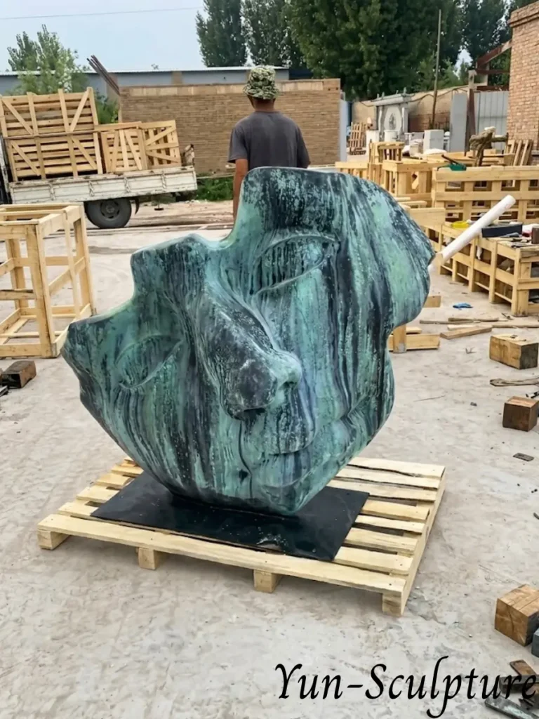 A monumental bronze face fragment with a detailed green patina, shown on a shipping pallet at the Yun Sculpture foundry. This large-scale modern artwork demonstrates our ability to translate facial features into massive architectural statements.
