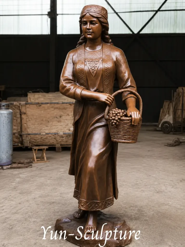 A life-size cast bronze statue of Hebe, the cupbearer, holding a detailed basket of grapes. The structural strength of bronze ensures the integrity of the projecting elements, making it perfect for permanent outdoor placement in garden dining terraces or pool areas.