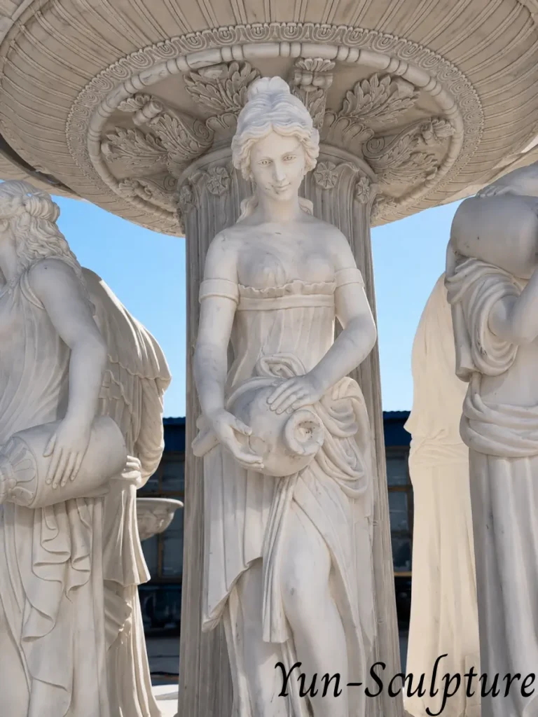 A close-up of a hand-carved white marble goddess figure holding an amphora on a tiered fountain. The sculpture captures the "grammar of Venus" arriving from water, with intricate drapery and refined stone modeling that highlights its native connection to the fountain basin.