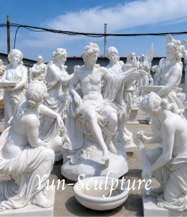 A promotional card on a blue background featuring a photo of a classical white marble sculpture group. The central figure is a seated male deity (representing Apollo or Bacchus), surrounded by several female figures in draped garments. A white cursive watermark reading "Yun-Sculpture" is overlaid on the image. Below the photo, the text reads: "Apollo & Bacchus - The Gods of Sun, Music, and Wine. Perfect for wineries and estates."