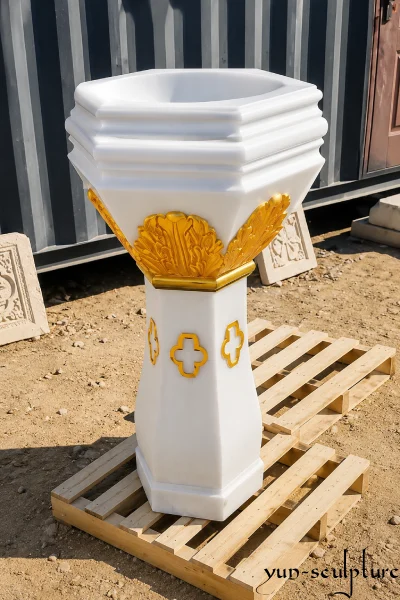 A hand-carved octagonal baptismal font made from a solid block of natural white marble, featuring elegant gold-leaf accents on the basin and stem. This sacred vessel is designed as a worthy "womb of the church" for Catholic sanctuaries, offering a permanent stone alternative to common fiberglass or concrete designs.