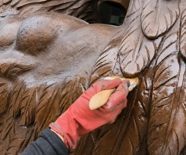 Protective surface treatment being applied by hand to the feather details of the bronze bluebird sculpture.