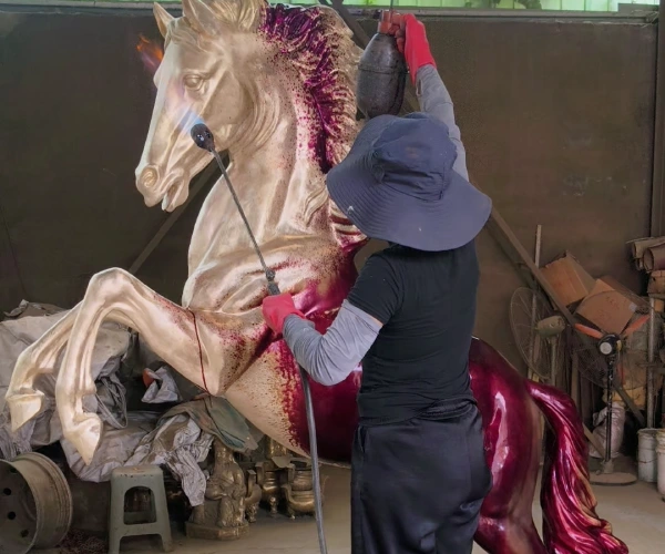 A Yun Sculpture craftsman applying patina by hand to the custom bronze horse sculpture during the final coloring process.