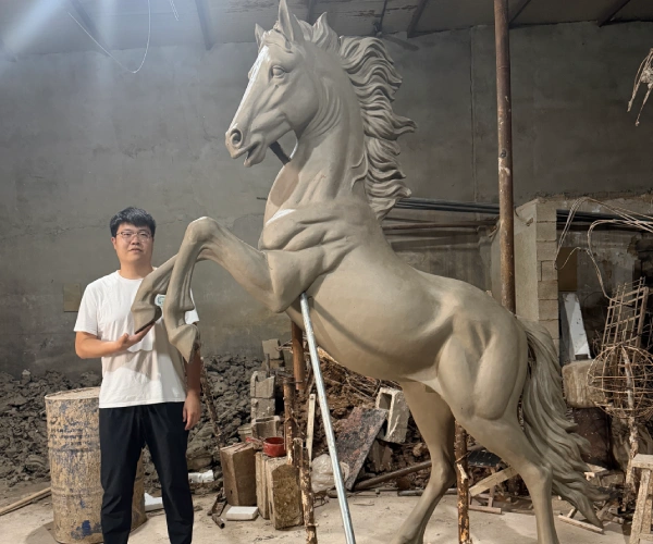Donghui Zhang, Owner of Yun Sculpture, standing beside the full-size clay model of a rearing horse sculpture for scale and proportion reference.