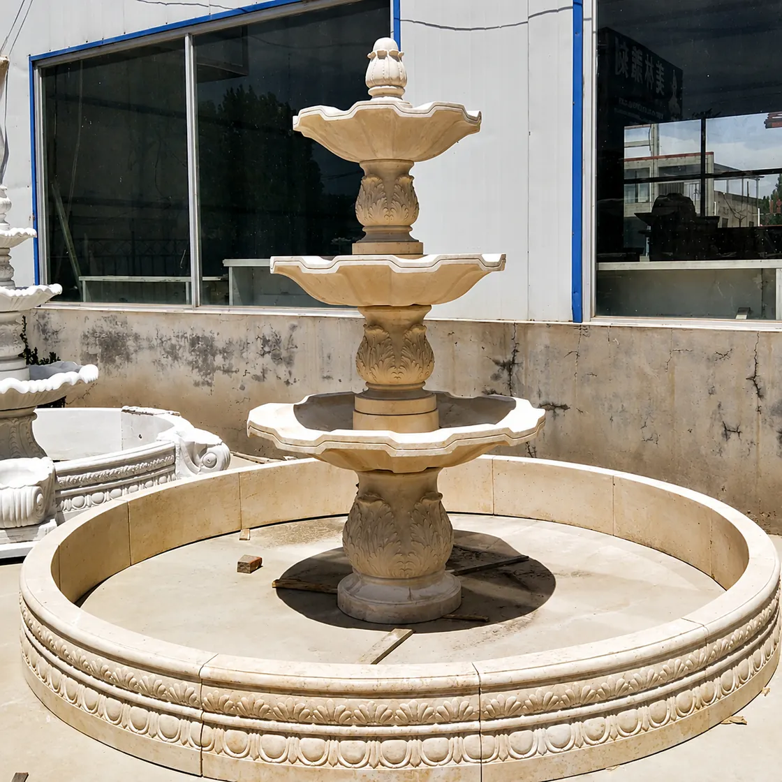 Beige natural stone three-tier fountain with circular carved basin in workshop