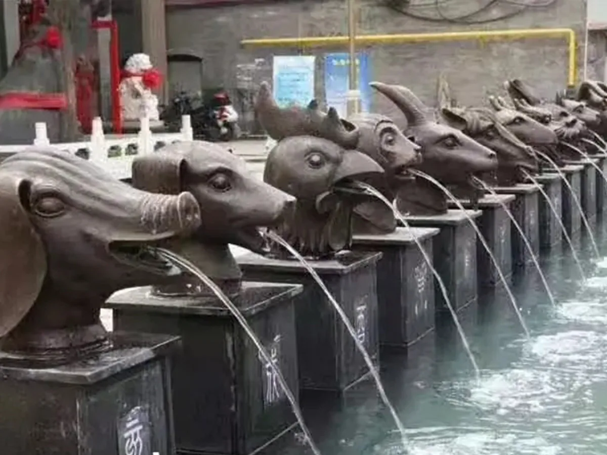 Row of varied bronze animal head fountain spouts running water into a pool