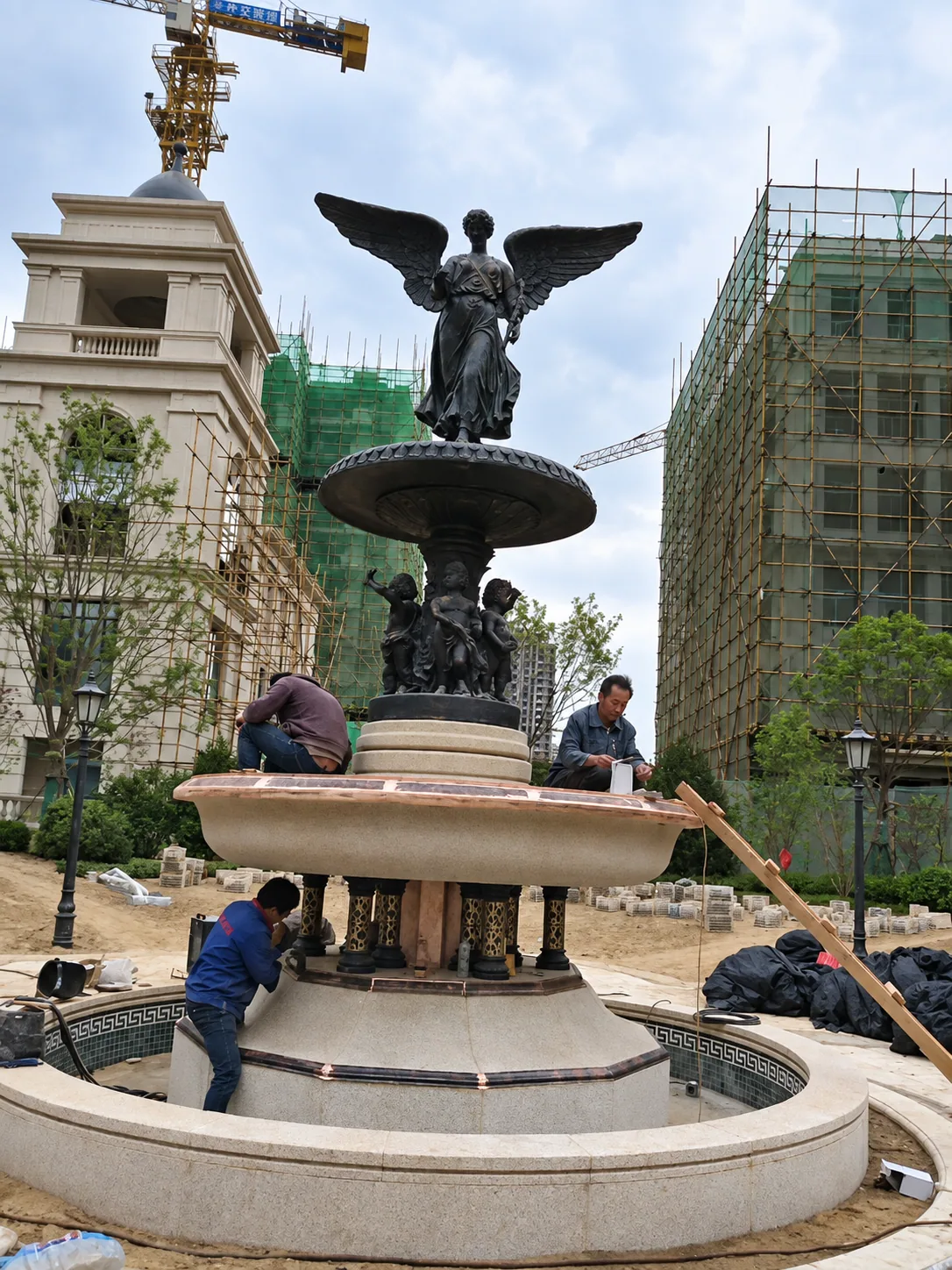 Workers installing a winged bronze angel and cherub fountain at a residential site