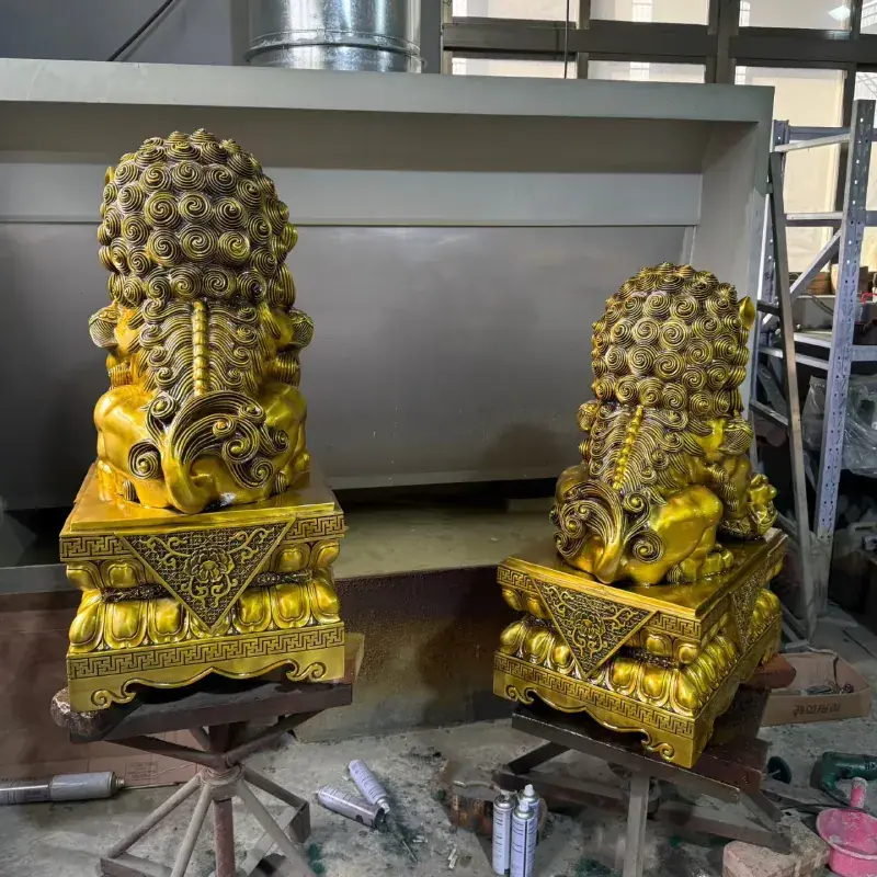 Rear view of a gold-patina bronze Foo Dog statue pair showing curled manes and bases