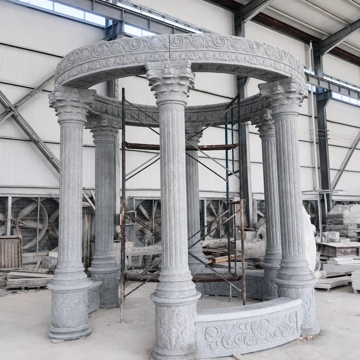 Gray stone round gazebo with carved columns and open top being assembled in the workshop