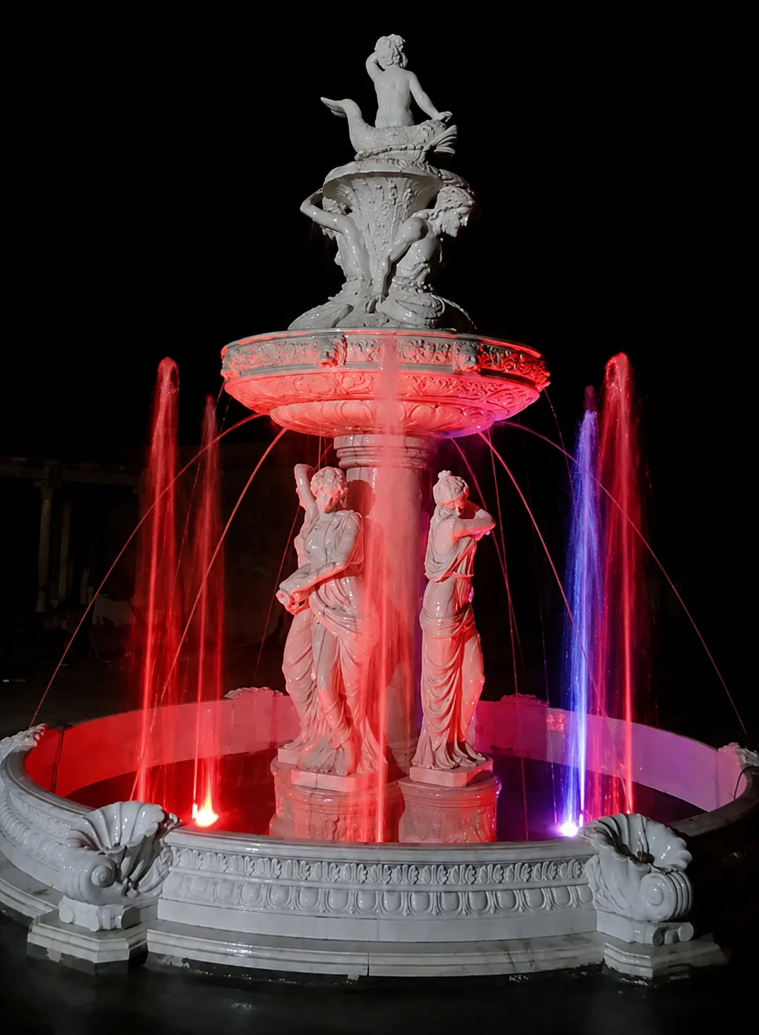 Classical white stone figure fountain running with illuminated water jets at night