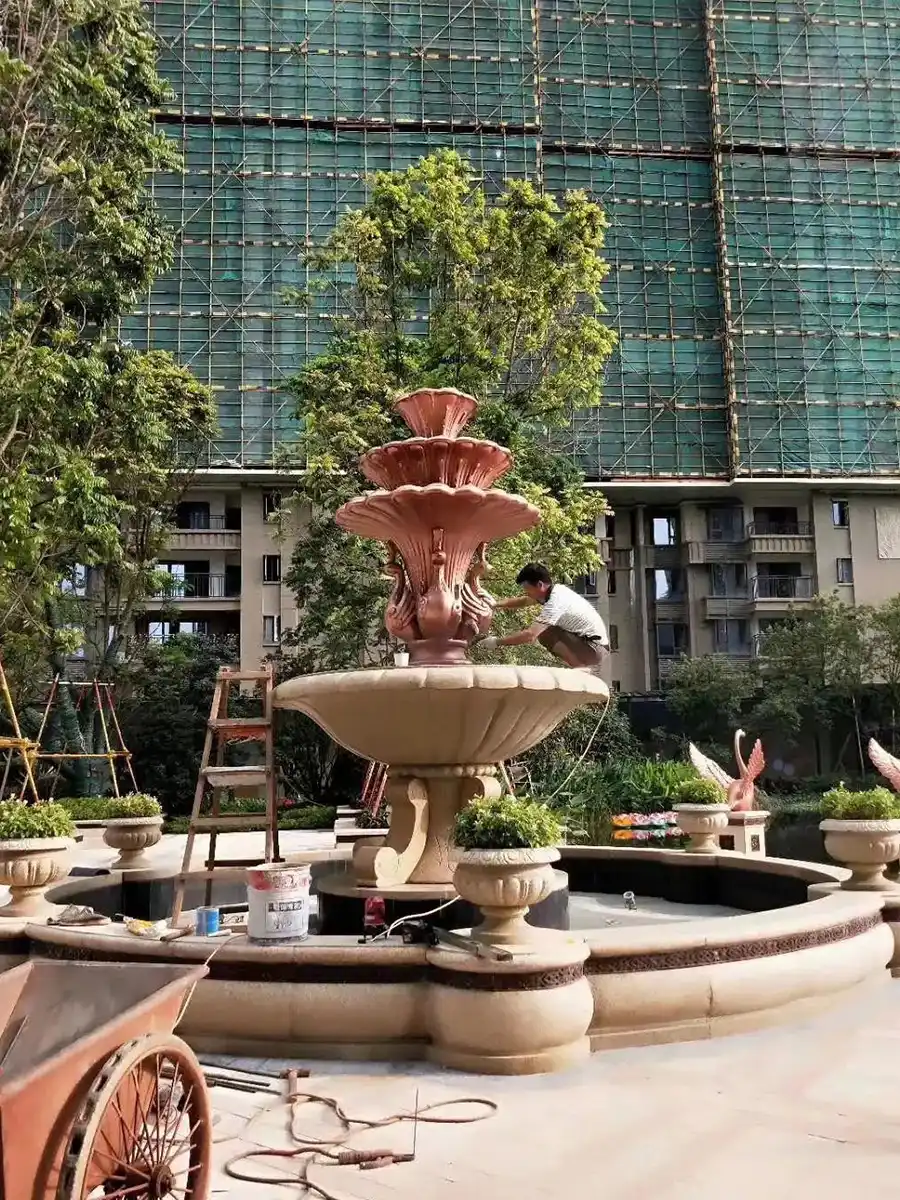 Pink metal shell tier fountain above a pale stone basin during garden installation