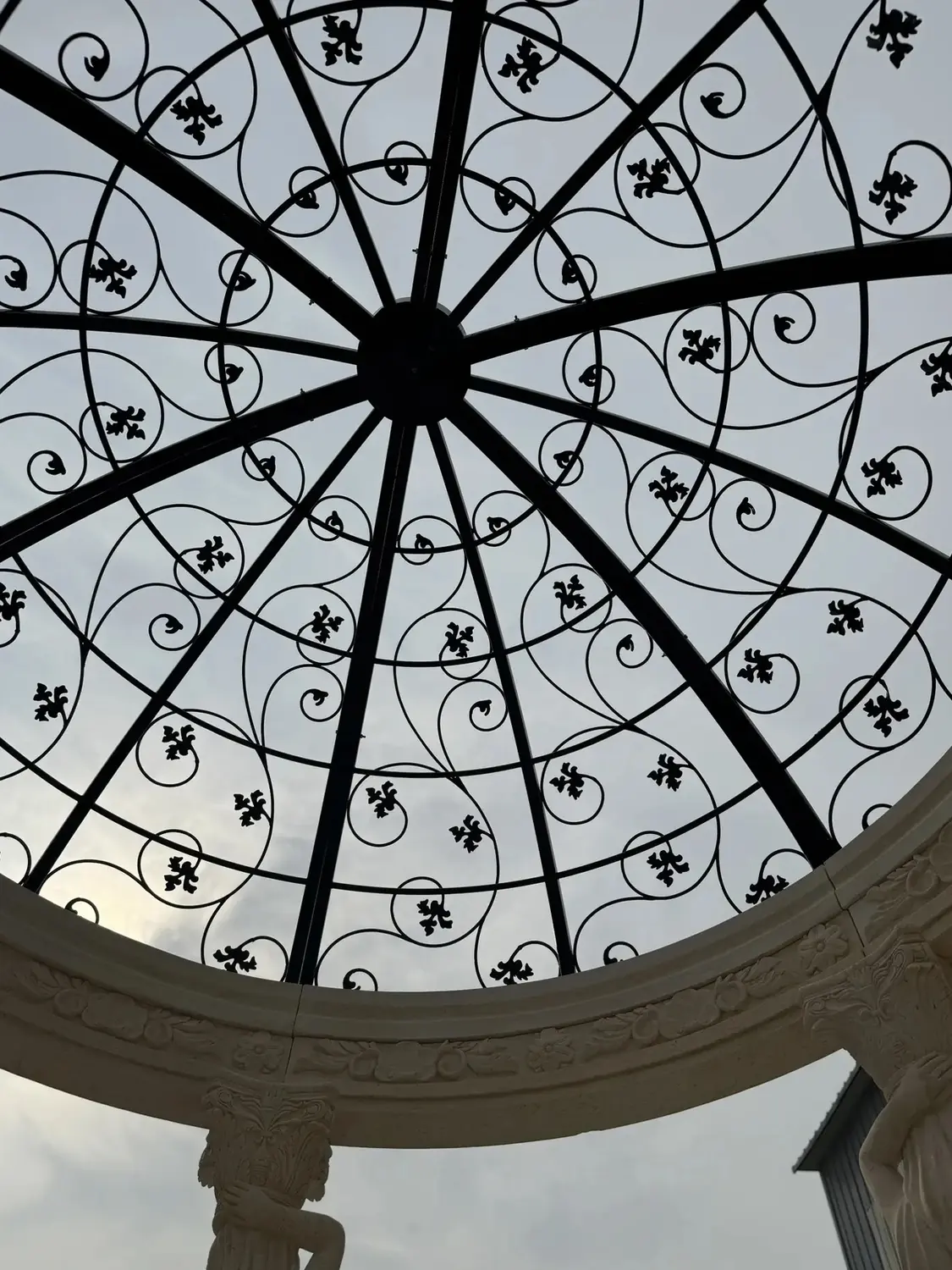 Looking up at the decorative wrought iron dome inside a marble gazebo