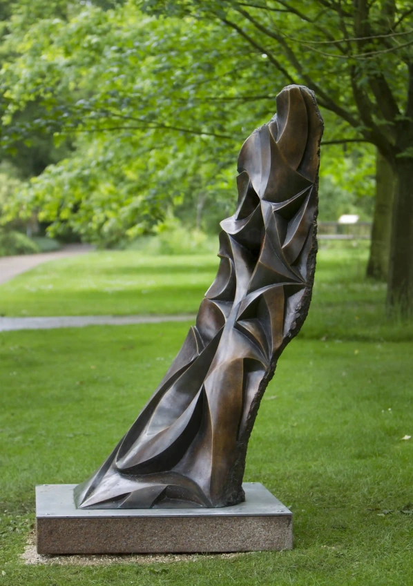 Abstract bronze dog sculpture with flowing planes displayed on a stone plinth in a green garden setting.