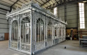 Silver-colored metal garden-room frame with arched bays and a raised roof feature in a workshop