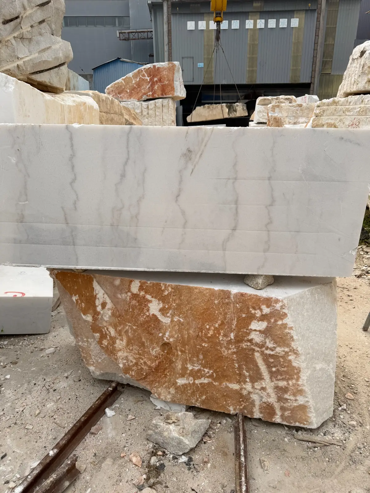 Pale rectangular stone block with gray veins standing on a larger block in a material yard