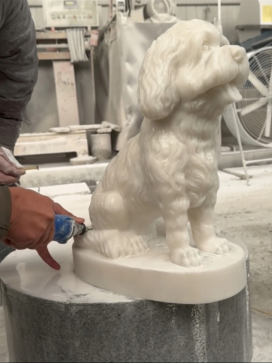 Worker using a handheld tool on a white marble seated dog sculpture with grouped coat detail and a round base.
